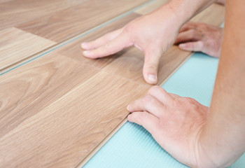 Contractor installing wooden laminate flooring with insulation and soundproofing sheets. Man laying...