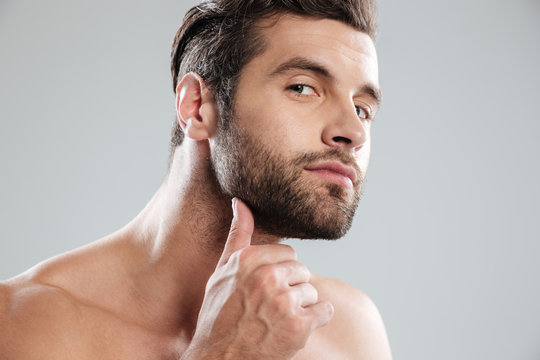 Portrait of a handsome naked bearded man examining his face