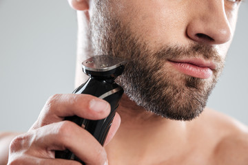 Cropped image of a young bearded man using electric shaver