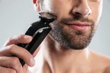 Cropped image of a bearded man using electric razor