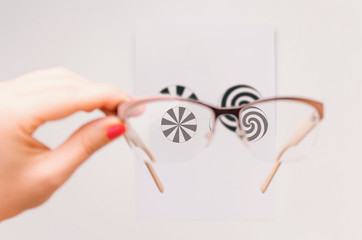 Woman's hand holding eyeglasses and checking for astigmatism - obrazy, fototapety, plakaty