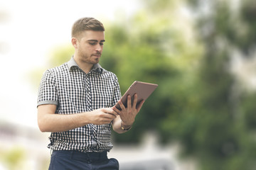Young man casual dressed using tablet to look for information or book hotel. Bokeh background.