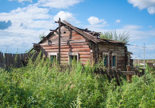 Old wooden dilapidated rural house stands in a thicket of bushes and grass. Abandoned building.