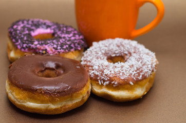 Delicious donuts with chocolate, coconut and pink glazed, with an orange cup of chocolate in a wooden background