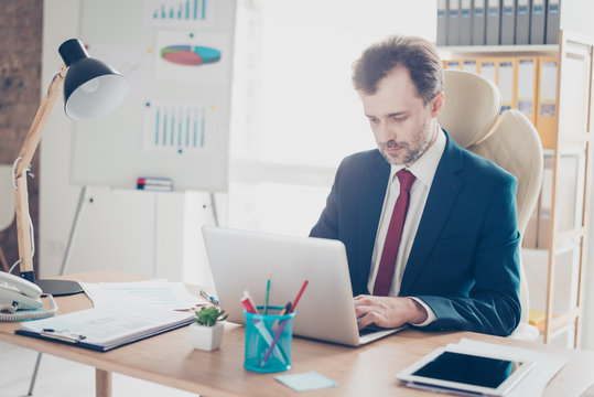 A portrait of busy man typing at his laptop in the modern office. He is wearing formalwear and concentrated at project