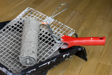 Painting supplies on wooden background. Painter tools in black tray with grey paint, roller brush and paintbrush.