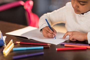 Cropped shot of cute little girl sitting at table and drawing with felt tip pen, doing homework concept