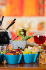 Delicious kiwi in a metal stick with assorted fresh fruits inside of bowls with red wine in a cup on wooden table