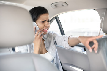 angry african american woman using smartphone in taxi