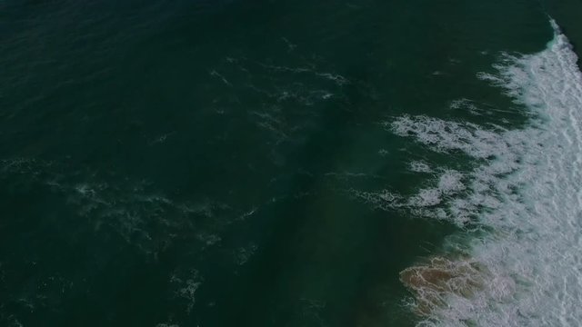 aerial footage of the English coast with rocky cliffs and breaking waves, camera panning up from water