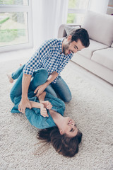 Excited young couple is fooling around and plays indoors at home, at a cozy beige carpet, wearing...