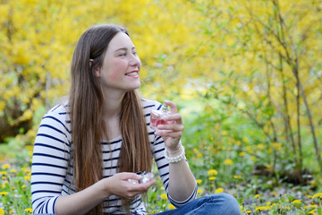 Beautiful young woman holding perfume sitting in the park, natural background.