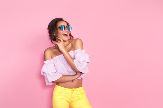 Beautiful girl in colorful clothes wearing sunglasses posing on pink background in studio.