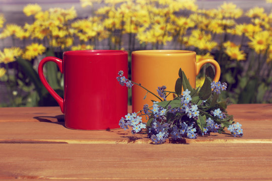 coffee break with a summer mood/ Red and orange mug with a blue bouquet of flowers on a street table 