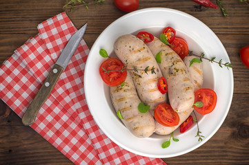 Boiled grilled sausages with cherry tomatoes and chili peppers with greens. Wooden background. Top view. Close-up