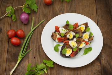 Baked eggplant with bacon, garlic and quail eggs. Wooden background. Top view. Close-up