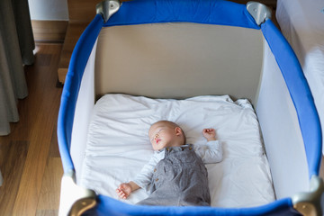 Cute little Asian 1 year old toddler baby boy child sleeping in baby cot near parent's bed in bedroom, Peaceful kid lying on baby bed while sleeping, Daytime sleep concept (shallow depth of field)