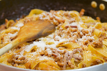 A pan with fettuccine al ragù and parmigiano cheese and a wooden spoon.