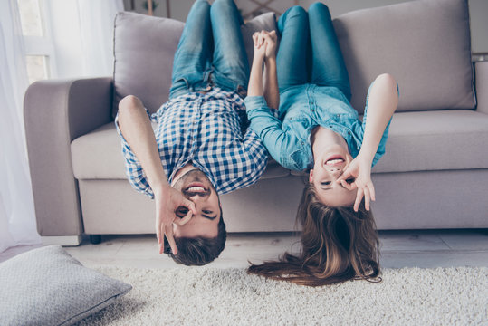 Funny couple with glasses gesturing is lying upside-down on the sofa at home. They are so cheerful, having fun together, go crazy, brother and sister