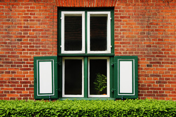 Fragment of a building with windows of an old palace of red brick. Before the window, decorative bushes
