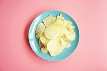 Potato chips on blue plate on pink background. Top view with copy space.