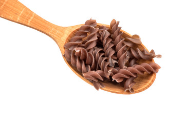 Dark raw fusilli pasta in spoon on white background, closeup