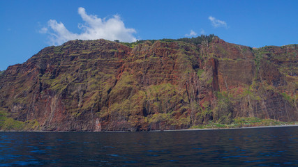 Madeira - Giant red cliffs and blue sky and ocean water from boat beneath Cabo Girao