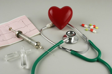 Stethoscope, syringe, electrocardiogram and red heart on gray background.