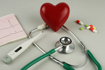 Stethoscope, electrocardiogram, thermometer, and a red heart on a gray background.