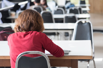 Asian female student Glasses and red robes are sitting, writing notes with pencils about studying at university libraries, in selective focus.