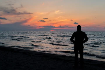 Gardinen Jurmala (Riga), Latvia - April 27, 2017: A person standing in golden light during sunset on the sea shore. Silhouette of man watching over the sea. © RusskyMaverick