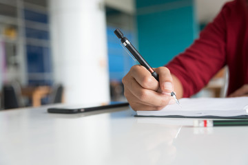 Asian female student Glasses and red robes are sitting, writing notes with pencils about studying at university libraries, in selective focus.