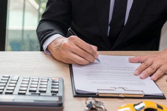 Businessman signing car loan agreement contract with car key and calculator on wooden desk.