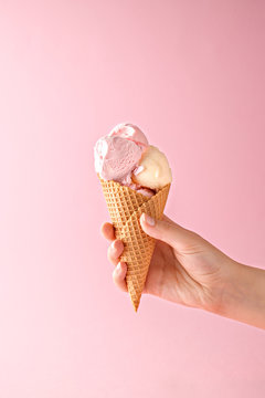 Naklejki Woman hand holding an ice cream cone on a pink background. 