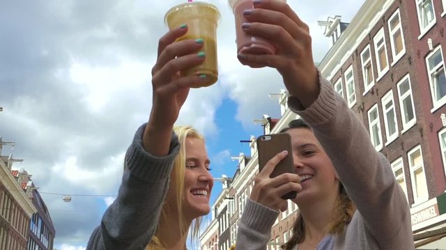Friends Take A Photo Of Their Colorful Smoothies In A Marketplace In Amsterdam, Netherlands