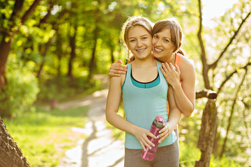 Beautiful sporty mother hugging and smilling with her charming daughter after jogging in summer park. Family, Love And Healthy lifestyle concepts