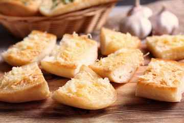 Tasty bread slices with garlic and cheese on wooden cutting board