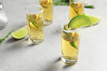 Golden tequila shots with juicy lime slices, rosemary and salt on light background