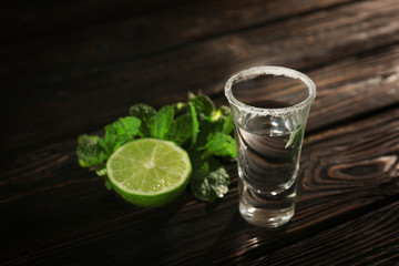 Tequila shot with juicy lime and salt on wooden background