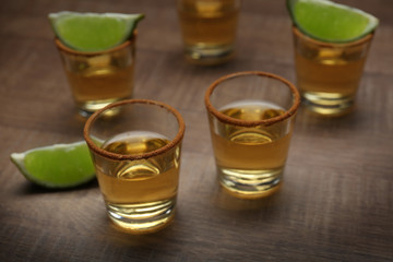 Golden tequila shots with lime on wooden background
