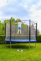 teen jumping on a trampoline against the backdrop of lush green of summer