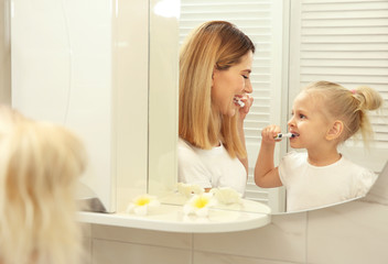Obraz na płótnie Canvas Cute little girl with her mother brushing teeth near mirror in bathroom