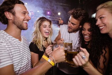 Happy friends toasting beer mugs at nightclub