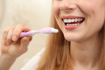 Smiling young woman with toothbrush on light background, close up
