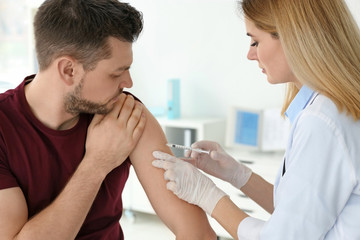 Vaccination concept. Female doctor vaccinating young man