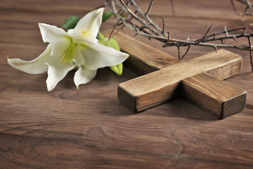 Crown of thorns, wooden cross and white lily on table