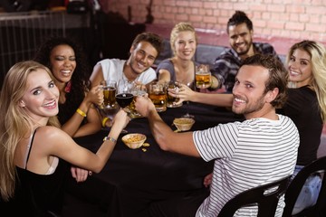 smiling friends toasting drinks while sitting together