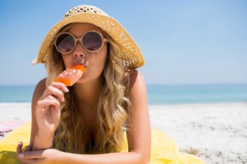 Woman eating popsicle while relaxing at beach - Powered by Adobe