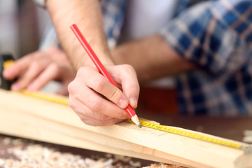 Carpenter applying marking onto wooden board in workshop, closeup