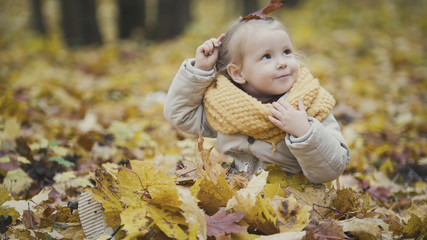 Little happy baby girl plays in autumn park among yellow leaves